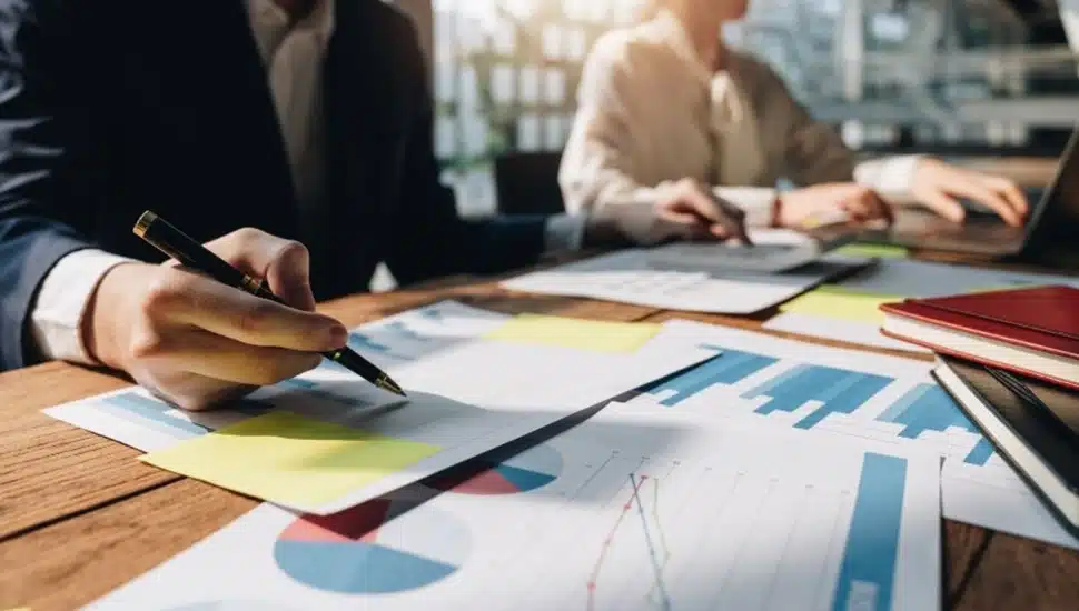 Business man and woman work at desk with charts and other documents.