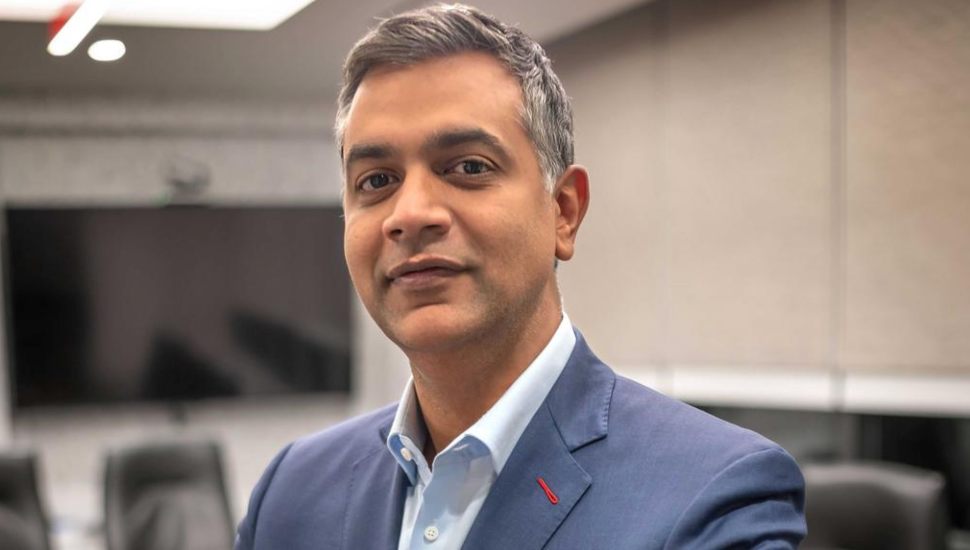 Sam Sidhu in a meeting room with TV and table behind him.