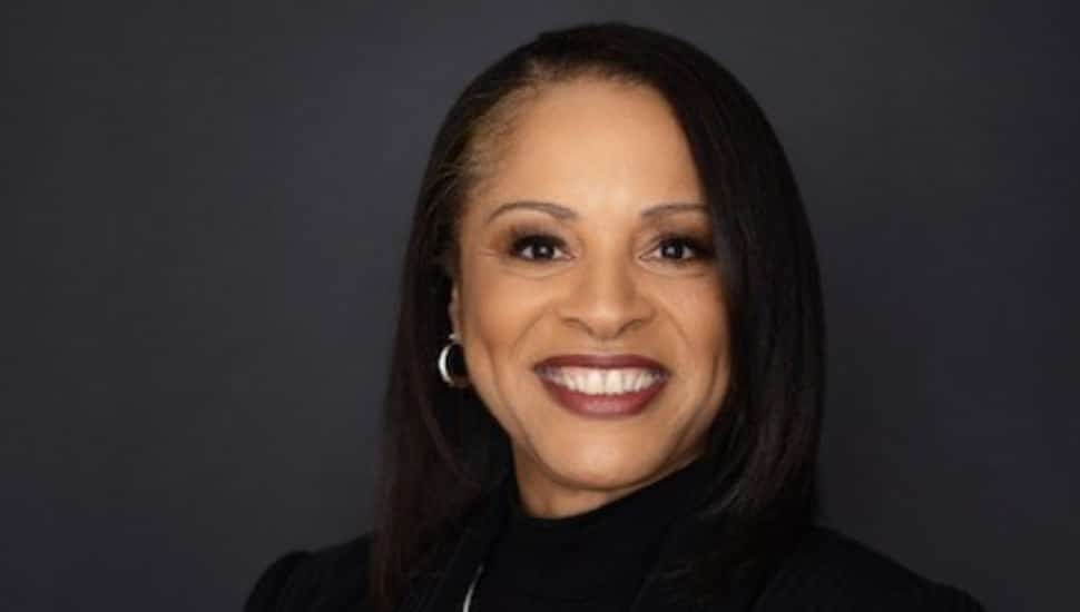 Celeste Warren. Celeste Warren smiling in a professional headshot against a dark background, wearing a black top and hoop earrings.