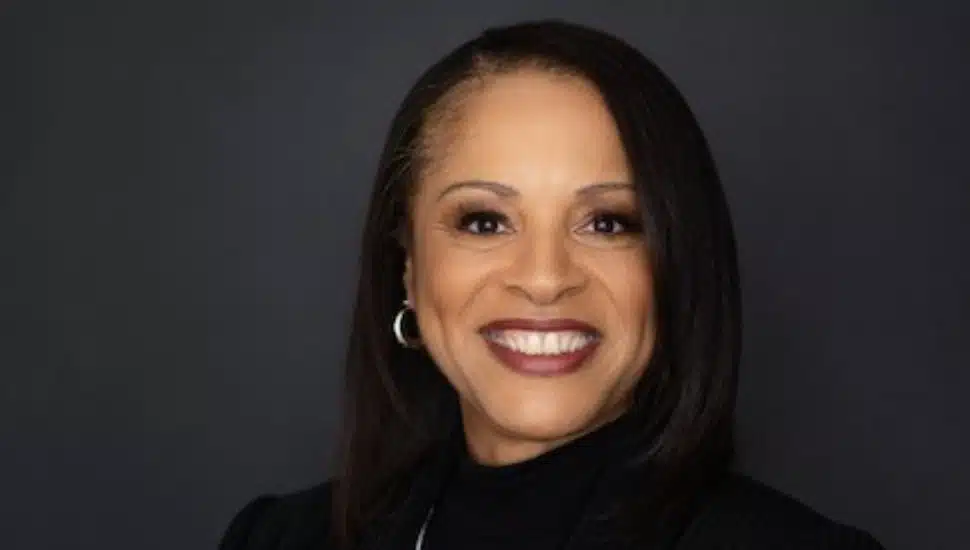 Celeste Warren. Celeste Warren smiling in a professional headshot against a dark background, wearing a black top and hoop earrings.