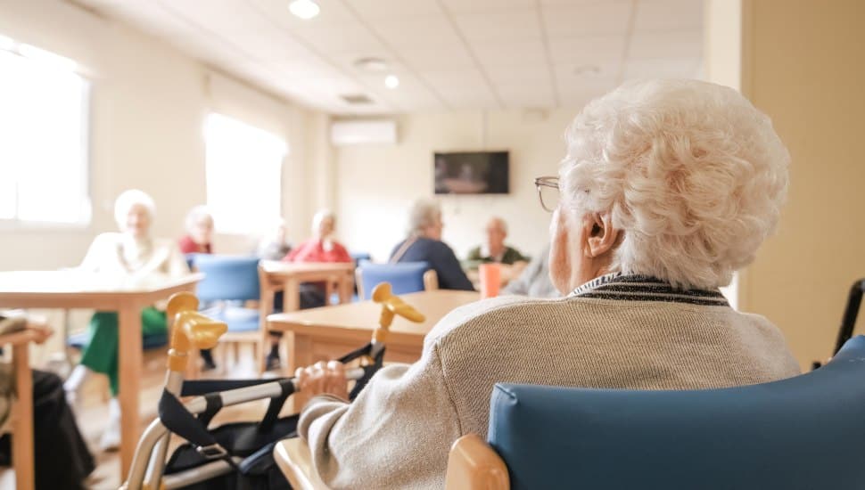 Back view of elderly woman with short white hair looking at others in nursing home.