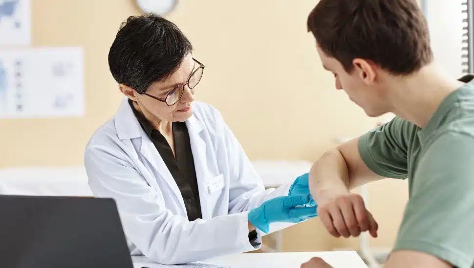 Female derm doc examining male patient's arm.