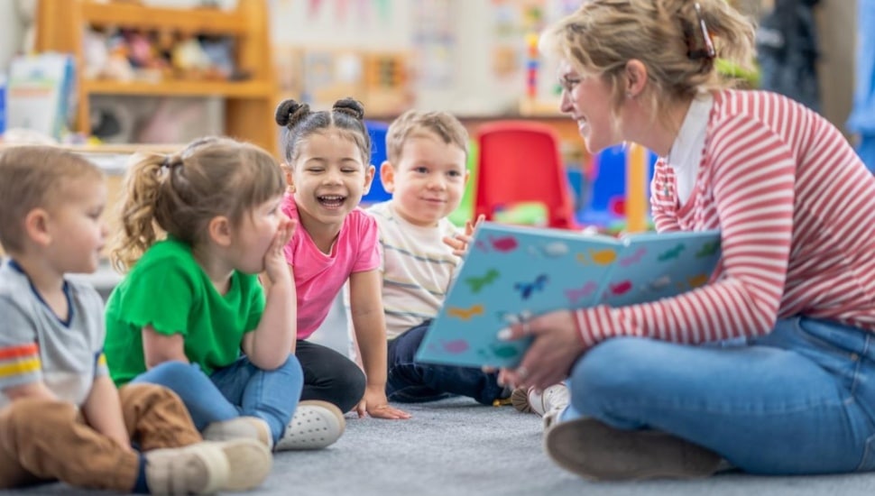 Female kindergarten teacher reads book to students at circle time.