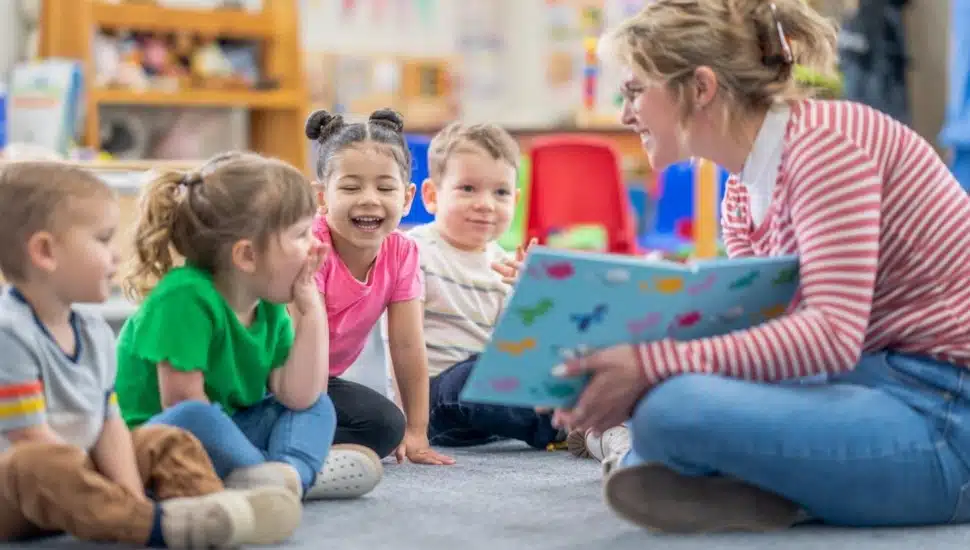 Female kindergarten teacher reads book to students at circle time.