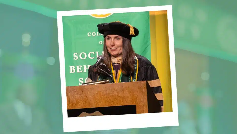Dr. Kate Gemma, wearing academic regalia and doctoral cap, stands at a podium speaking during Wilmington University’s 2025 commencement ceremony.