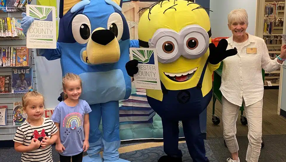 Children and adults posing with costumed characters at the Chester County Library Sign-Up Fest event.