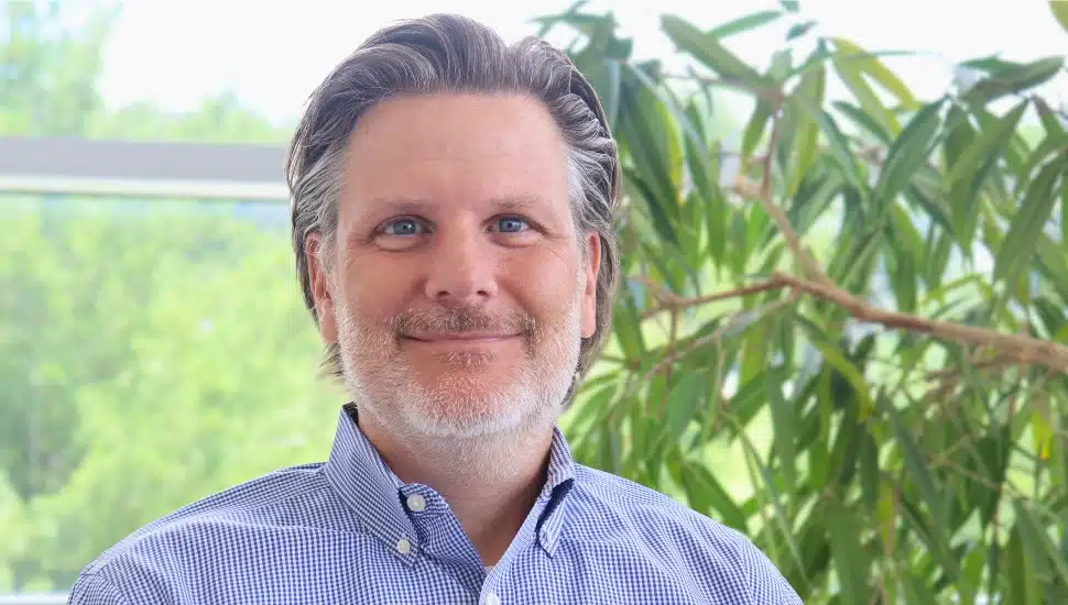 Headshot of middle-aged man with gray hair and beard in blue collared shirt.