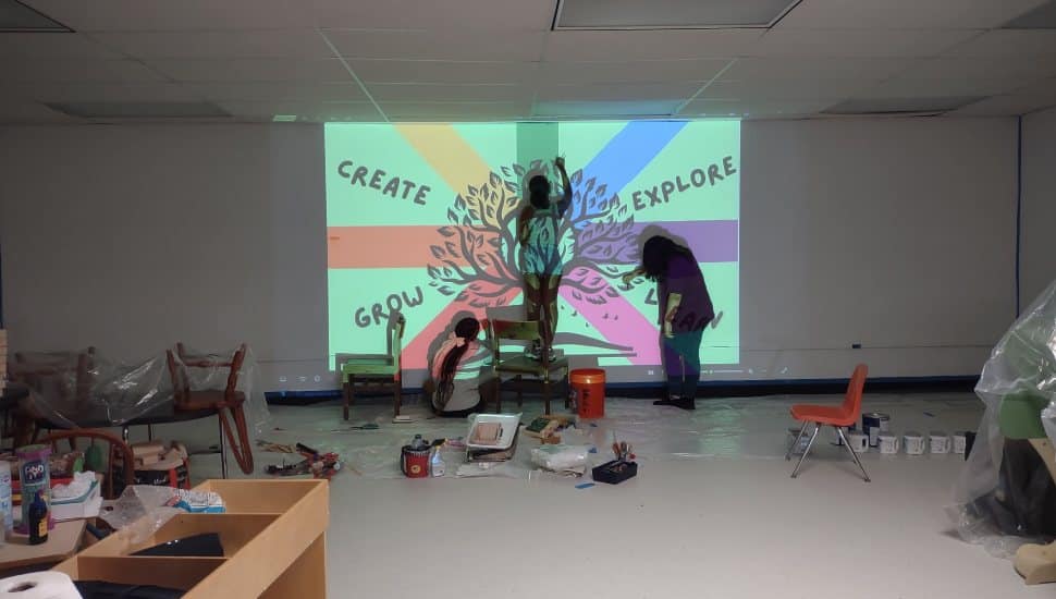 Volunteers painting a colorful mural with the words Create, Grow, Explore, Learn on the wall of the Coatesville Area Public Library Kids’ Zone.
