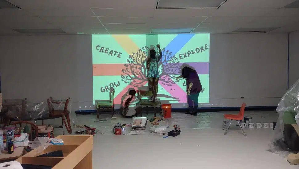 Volunteers painting a colorful mural with the words Create, Grow, Explore, Learn on the wall of the Coatesville Area Public Library Kids’ Zone.