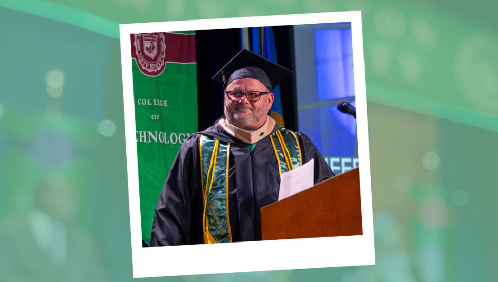 Paul Seiverd, wearing academic regalia with honor cords, stands at a podium delivering the 2025 commencement speech for the WilmU College of Business Undergraduate Programs Ceremony.