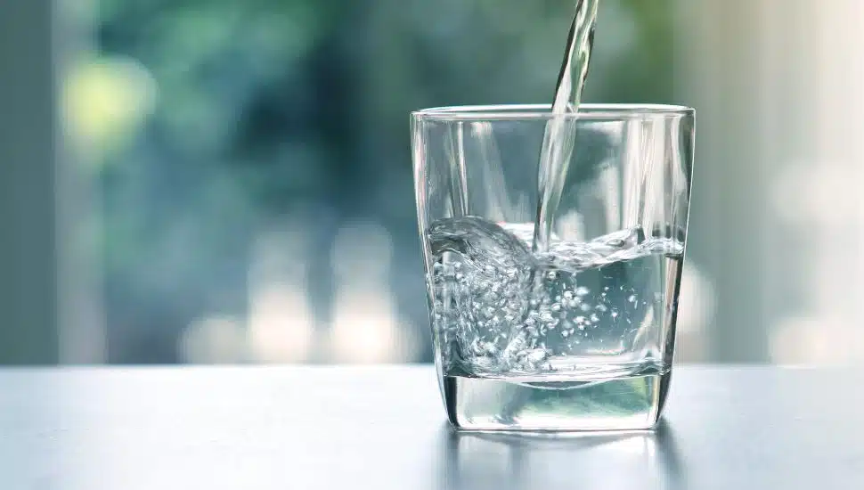 Close up pouring purified fresh drink water from the bottle on table in living room.