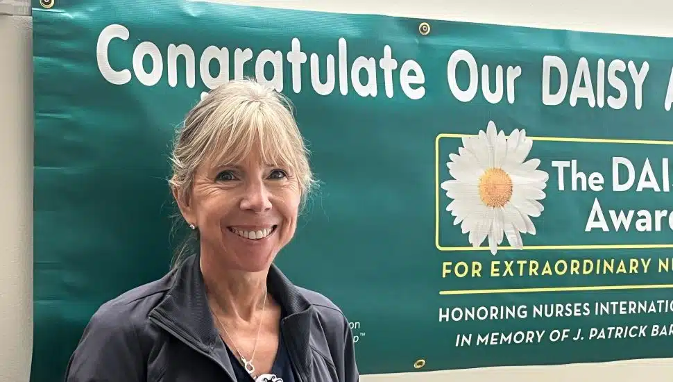 Nancy Maratea, RN, smiling in front of a DAISY Award banner at Chester County Hospital after receiving recognition for extraordinary nursing care.