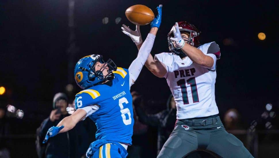 Two football players reach for ball in air.
