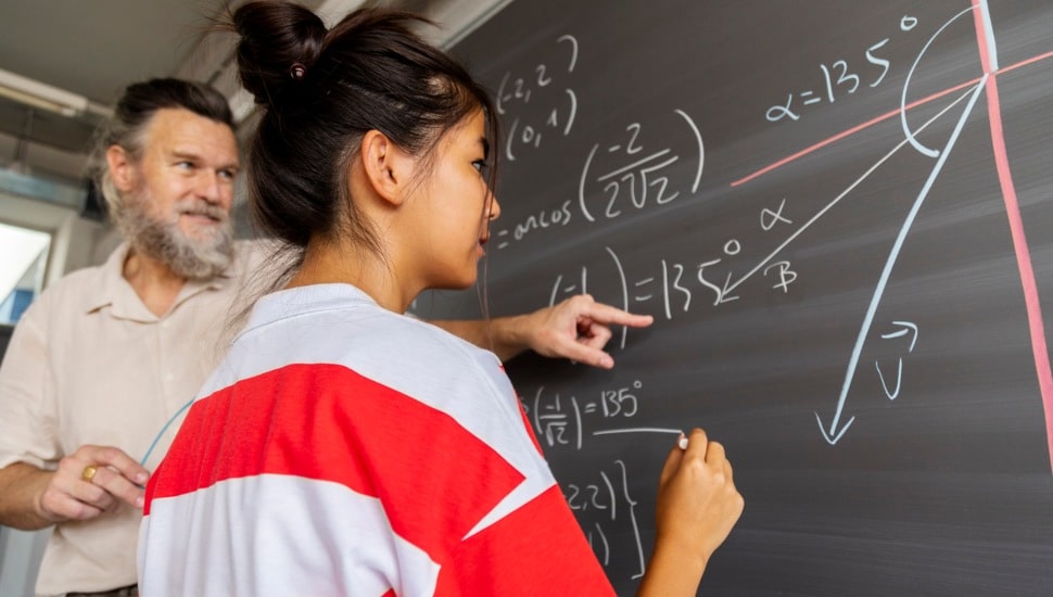 Student with teacher writing on chalkboard.
