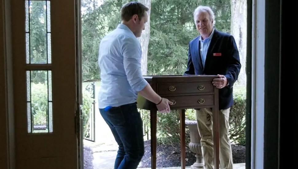 Two people carrying desk through doorway.