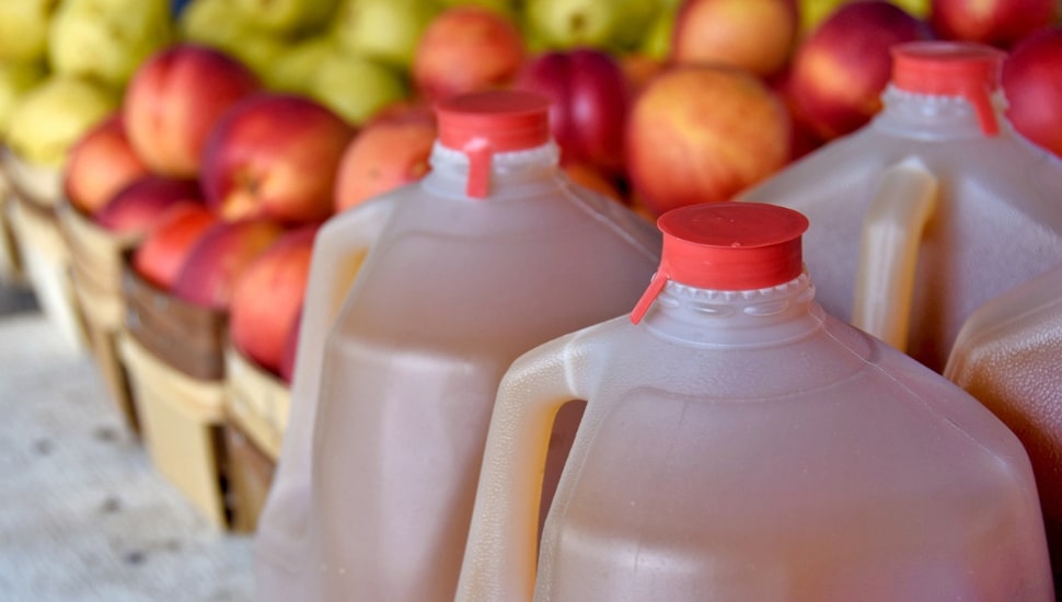 Several full apple cider gallons in front of red and green apples.