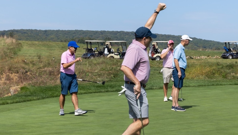 Men celebrate on green at golf fundraiser.