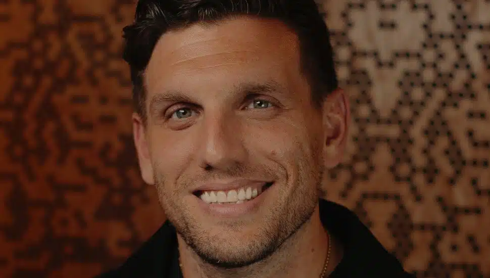 Comedian Chris Distefano smiling in a close-up portrait with a patterned background.