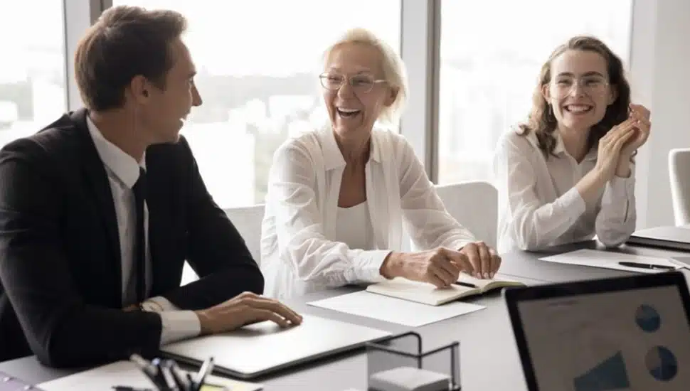 Corporate professionals smile at conference room table.