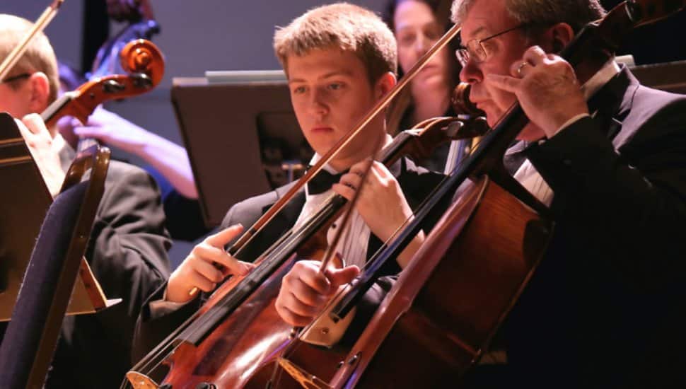 Musicians in the Immaculata Symphony performing on stage, with cellists in formal attire focused on their instruments during a concert.