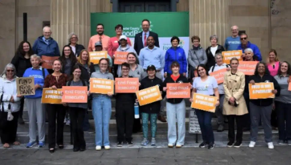 A large group of Chester County Food Bank supporters gather on the steps of West Chester’s historic courthouse during the 2nd Annual Rally Against Hunger. Participants hold orange and white signs reading “End Food Insecurity” and “Food is Not a Privilege” to raise awareness during Hunger Action Month.