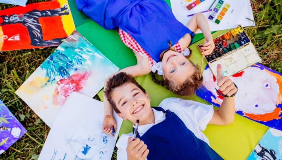 Children lie on the grass with their drawings next to them. kids on the ground with drawings.