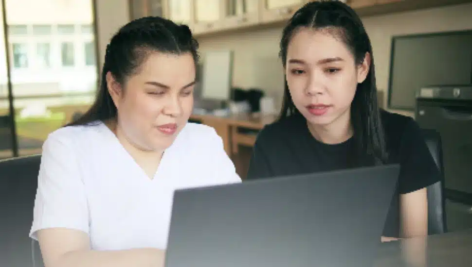 Two women take a virtual training course on a laptop.