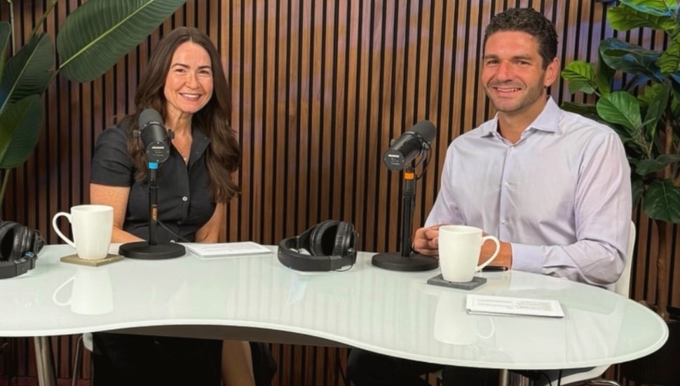 Two financial advisors sit at a desk on the set of their podcast.