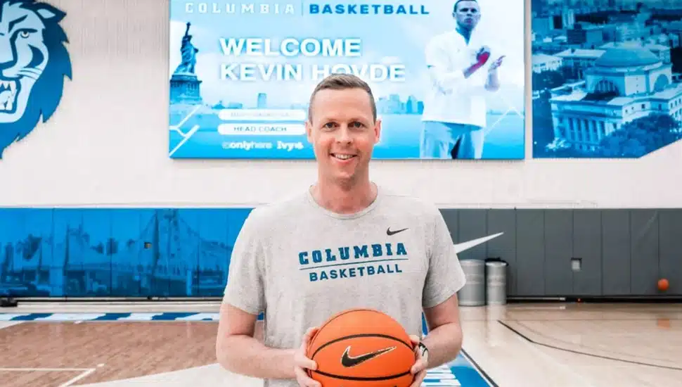 Male college basketball coach poses for picture in gym with basketball in hand.