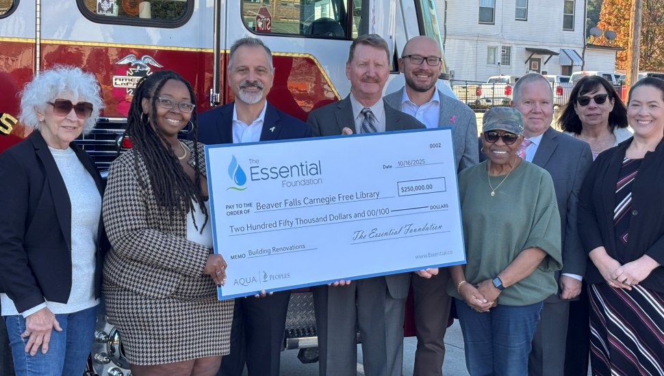 A group of community leaders and representatives from The Essential Foundation present a $250,000 donation check to the Beaver Falls Carnegie Free Library for building renovations, standing in front of a fire truck in Beaver Falls, Pennsylvania.