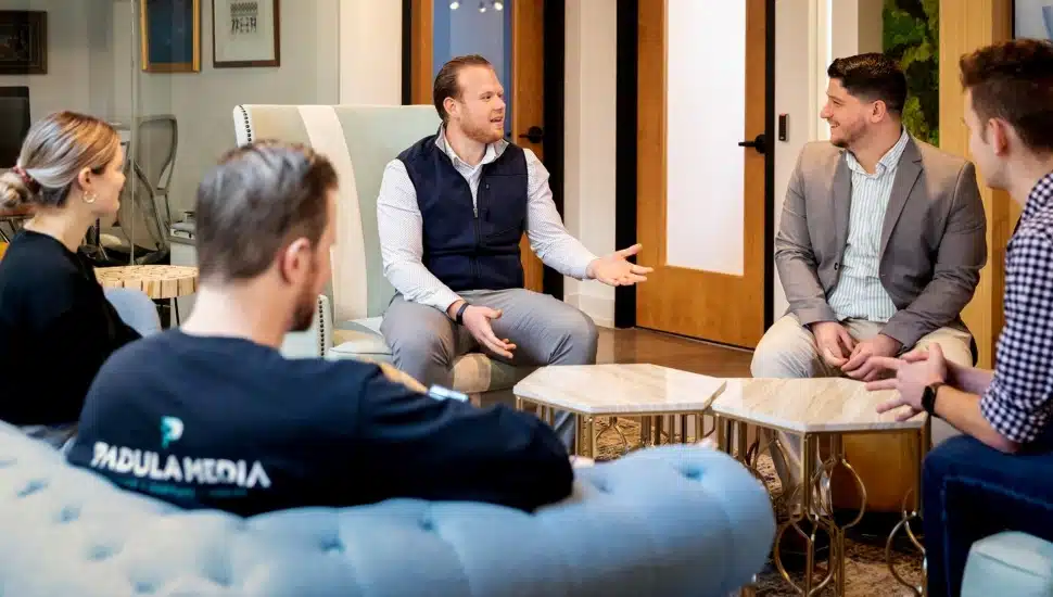 Young professionals discuss business in office common area.