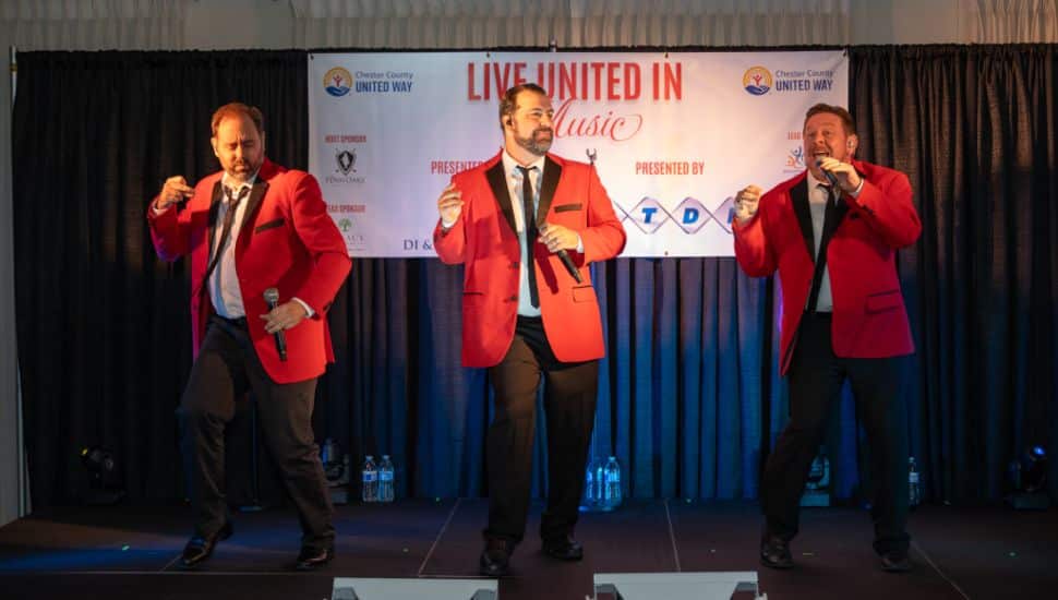 Three male singers on stage wearing red tuxes.