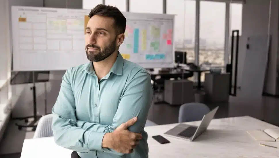 Thoughtful professional man stands with arms crossed in modern office.