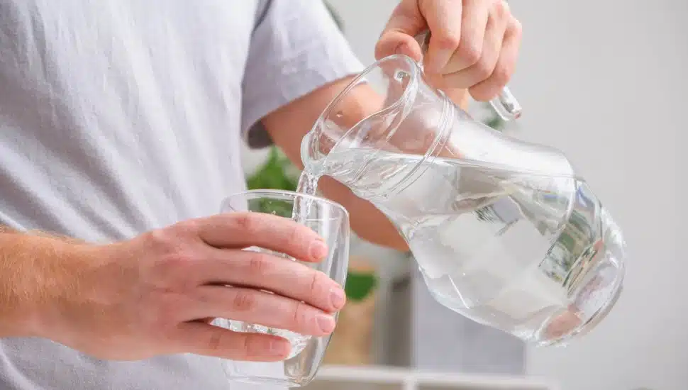 Man pours cold water into glass. Close-up of male hands pouring water from a jug into glass tumbler.