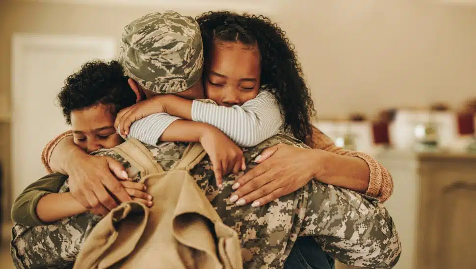 Soldier embracing his wife and kids on his homecoming. Serviceman receiving a warm welcome from his family after returning from deployment. Military family having an emotional reunion.