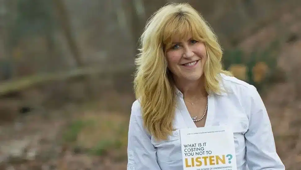 Christine Miles headshot holding her book with woods in background.