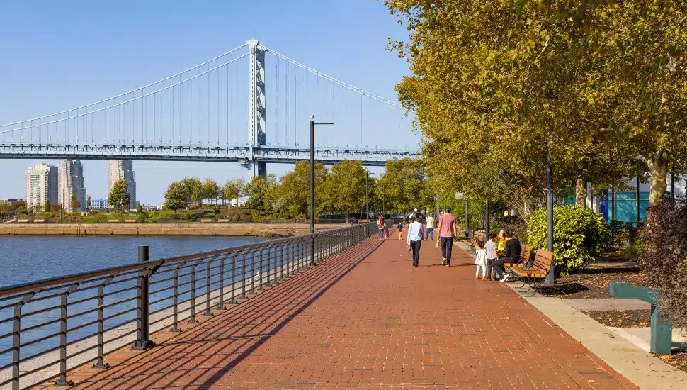 People walk on trail alongside river with bridge in background.