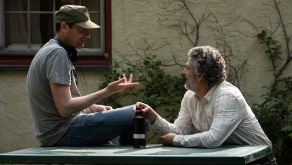 Brad Ingelsby and Mark Ruffalo talking at a table outdoors.