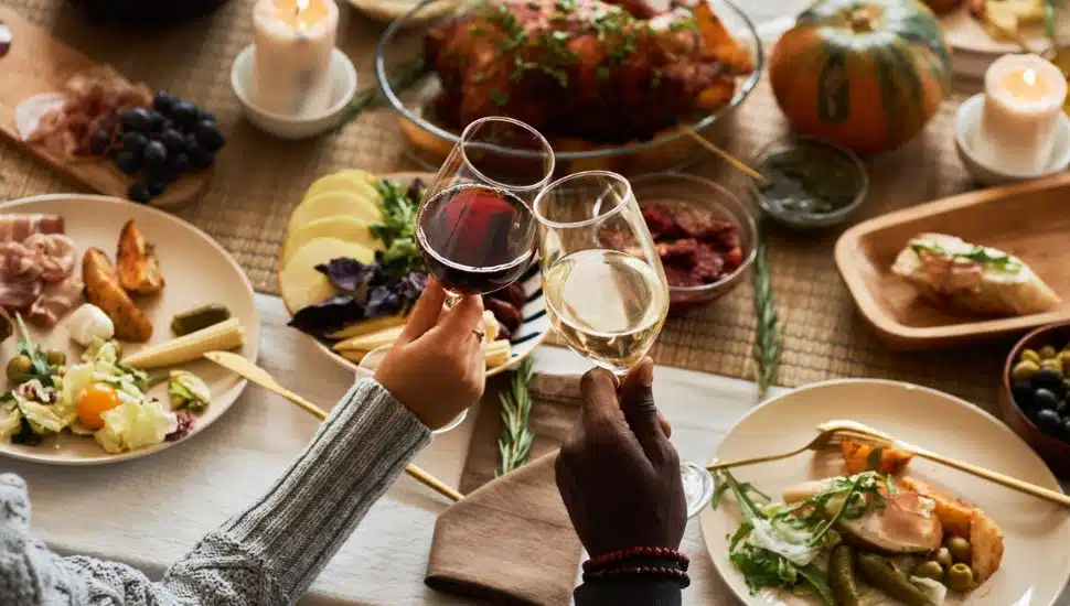 Two people toasting with wine glasses at festive Thanksgiving dinner table.