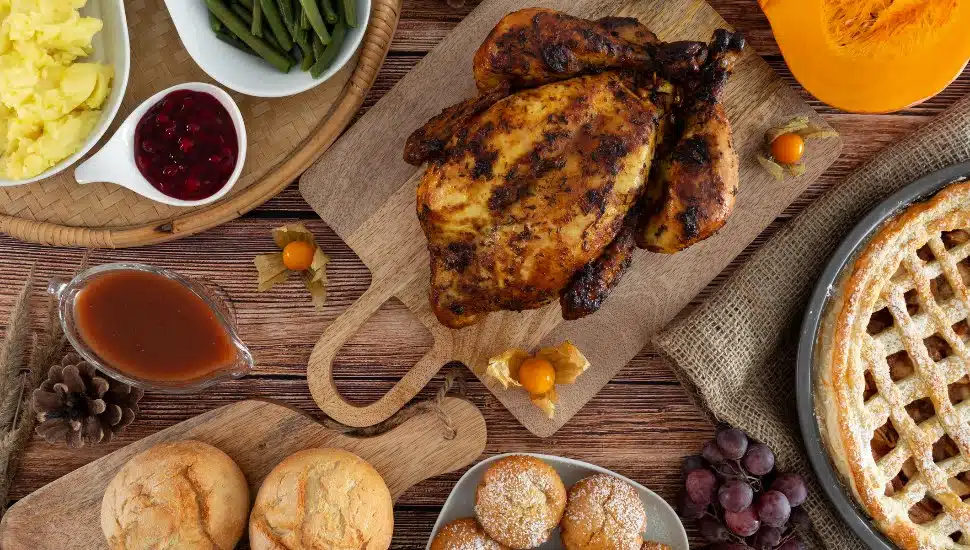 A Thanksgiving holiday table with a turkey, rolls, and desserts.
