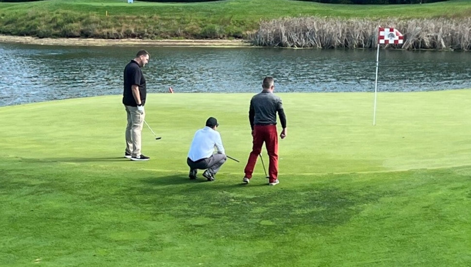 Three men putt on a golf course.