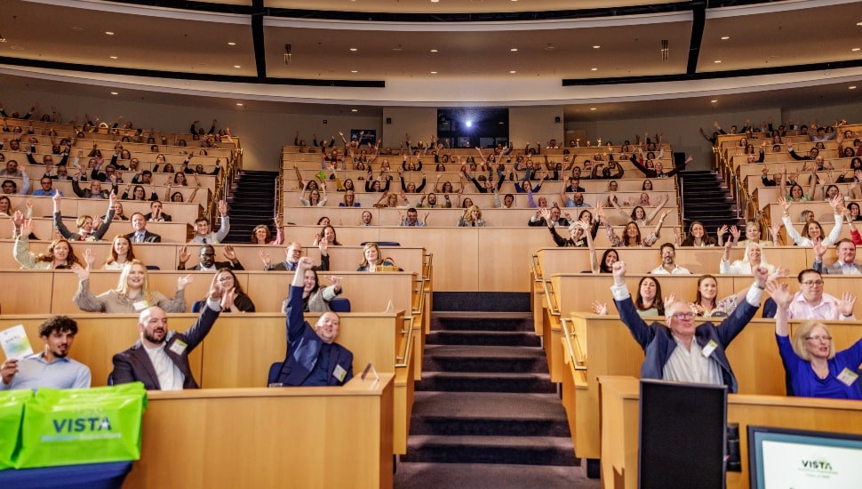 College lecture hall full of people with hands raised in triumph.