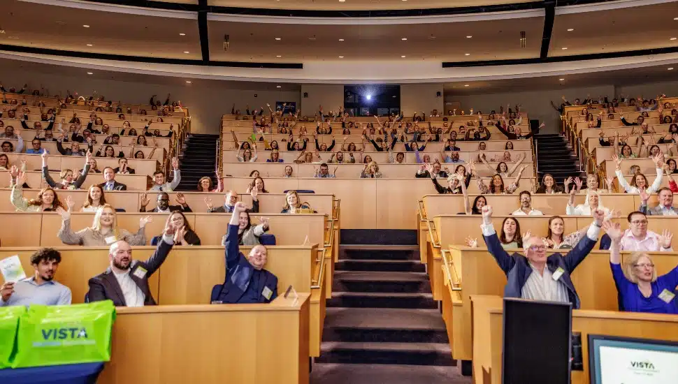 College lecture hall full of people with hands raised in triumph.