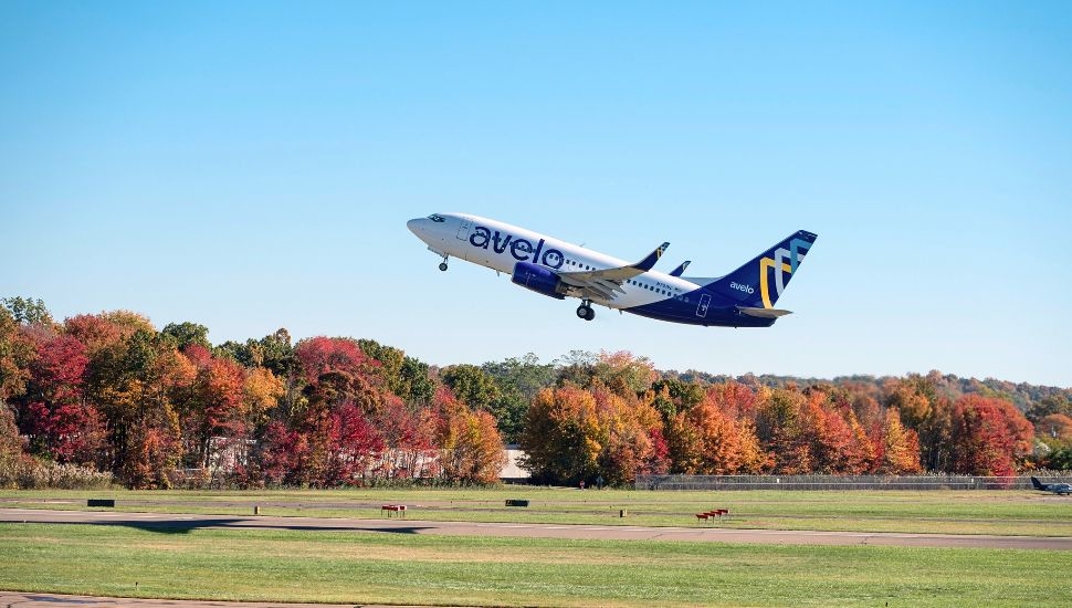 Avelo airplane taking off with fall foliage in background.