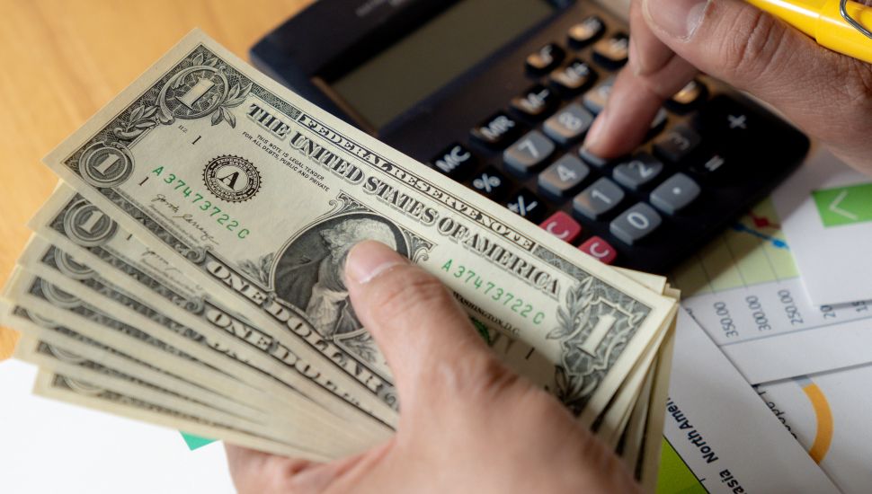 Person holding money and typing on calculator.