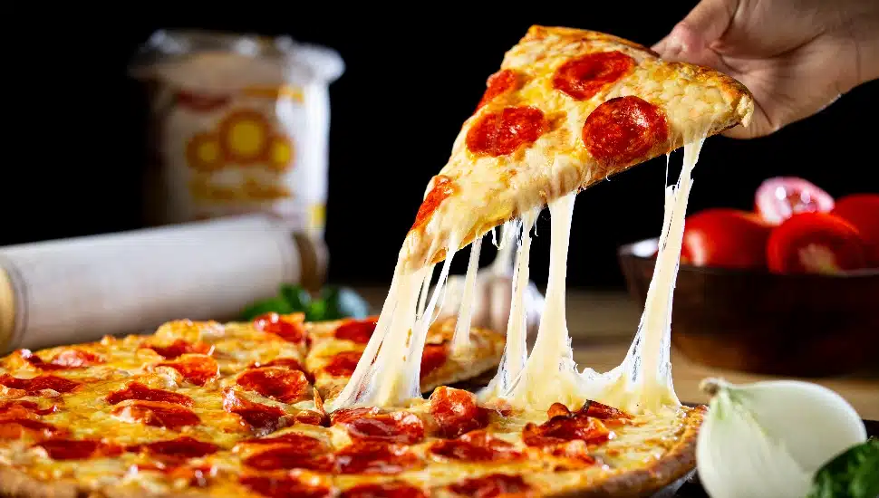 A person getting a piece of cheesy pepperoni pizza.