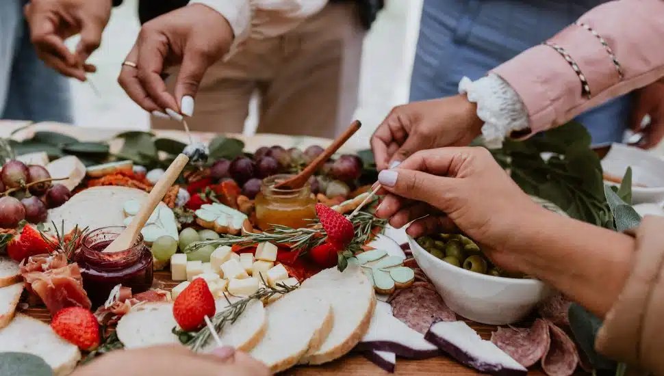 Several hands around a savory charcuterie board.