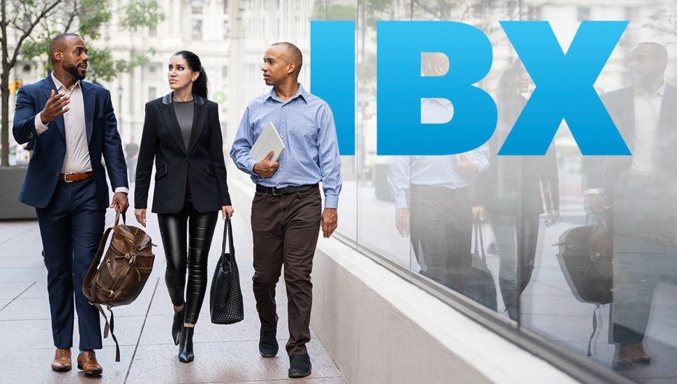 Businesspeople walk on sidewalk in big city next to letters IBX.