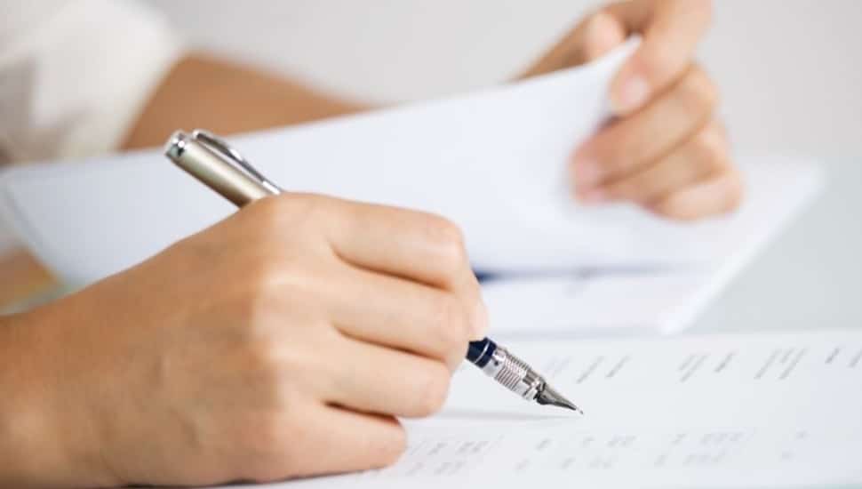 Hand holding pen writes on document.