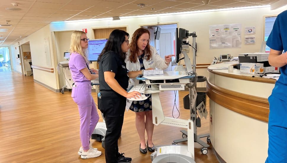 Family medicine residents and attending physicians collaborate at a mobile workstation inside Penn Medicine Chester County Hospital during clinical rounds following the transition of the former Crozer residency program.